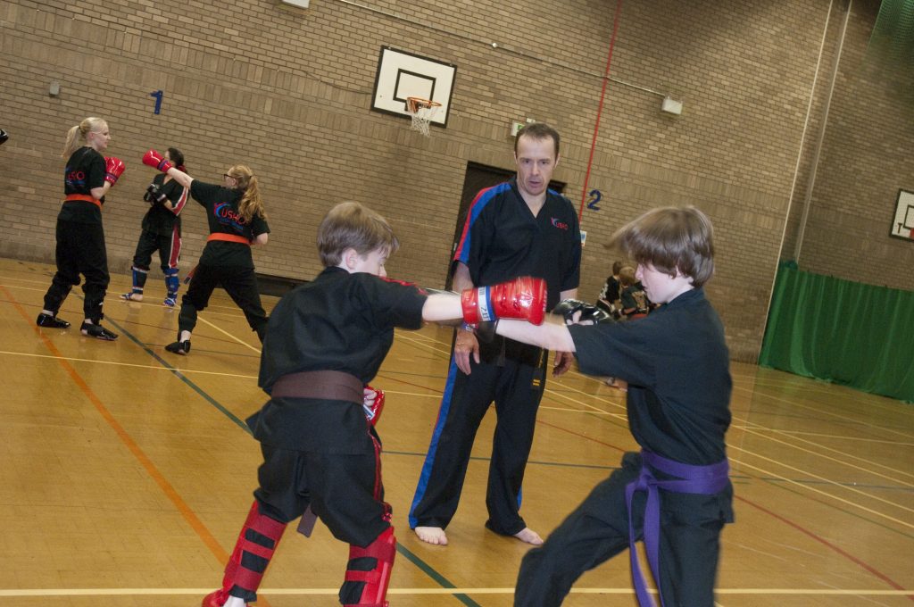Children sparring in a sports hall under an instructor’s supervision